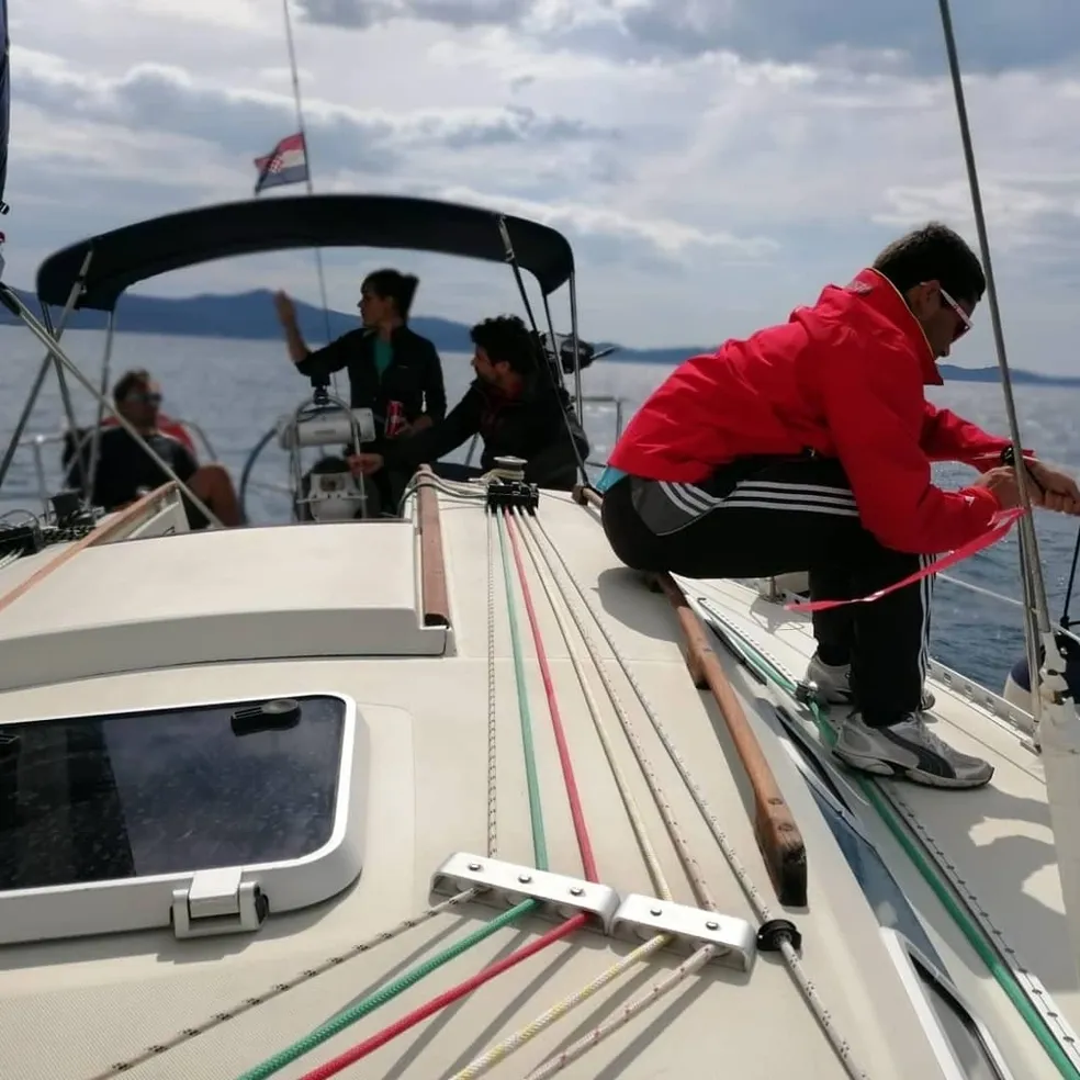 A man secures ropes to the bow of a sailboat at a sailing school in Zadar, Croatia, preparing for a sailing course.