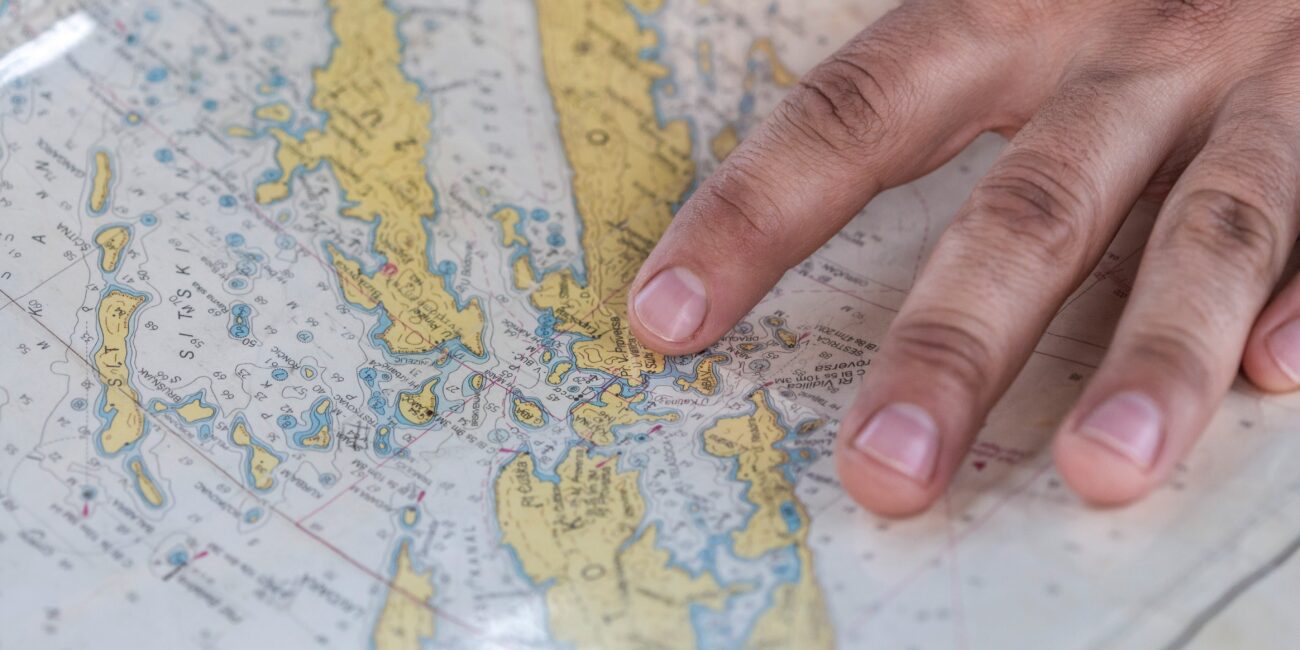 A hand rests on a map, indicating a location, symbolizing planning for sailing courses and professional skipper course in Zadar, Croatia.